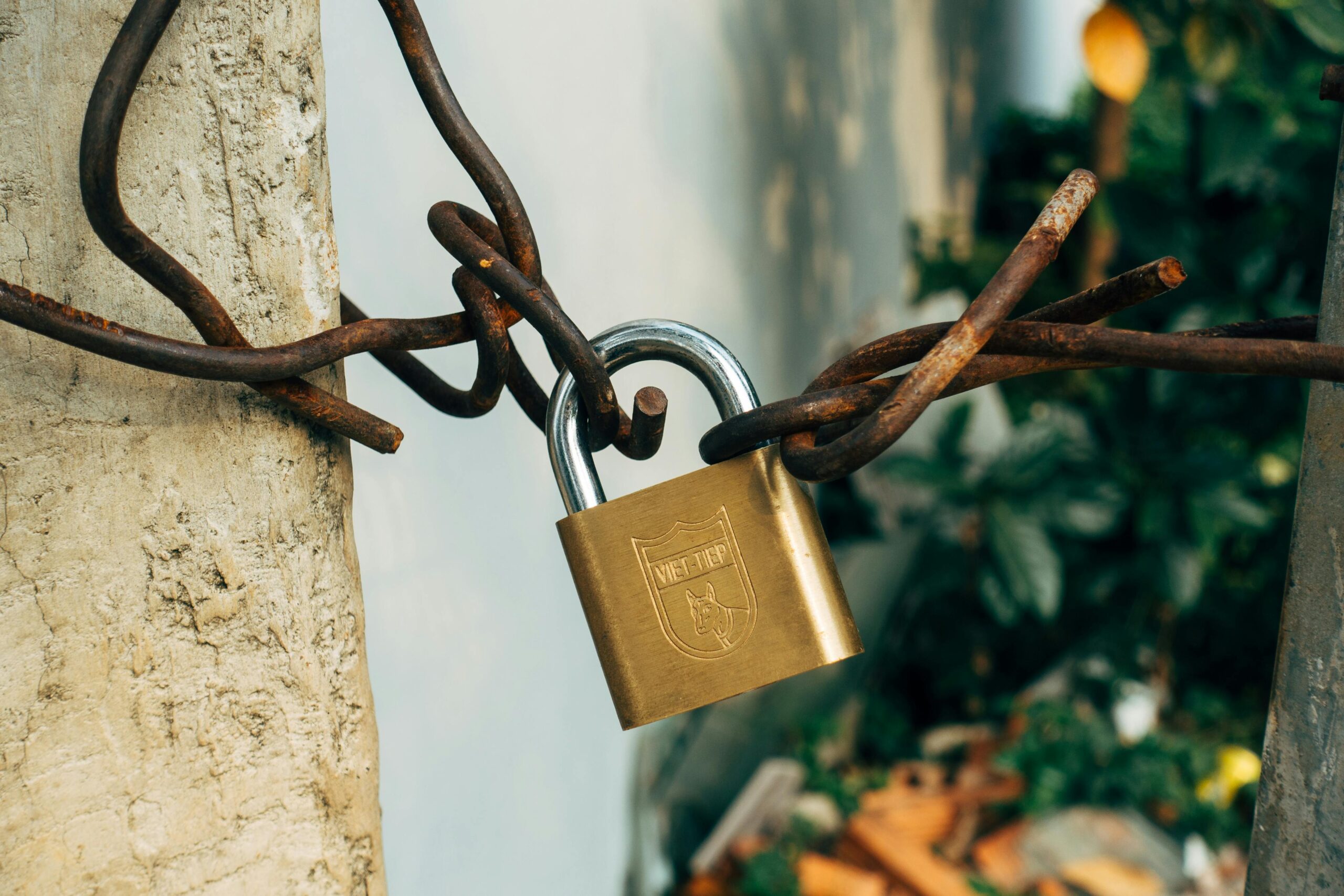 A brass padlock securing a rusty wire on a concrete post, symbolizing security and protection.