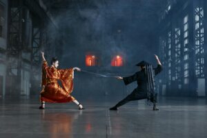 Two cosplayers in an intense martial arts face-off in a dramatic industrial setting.