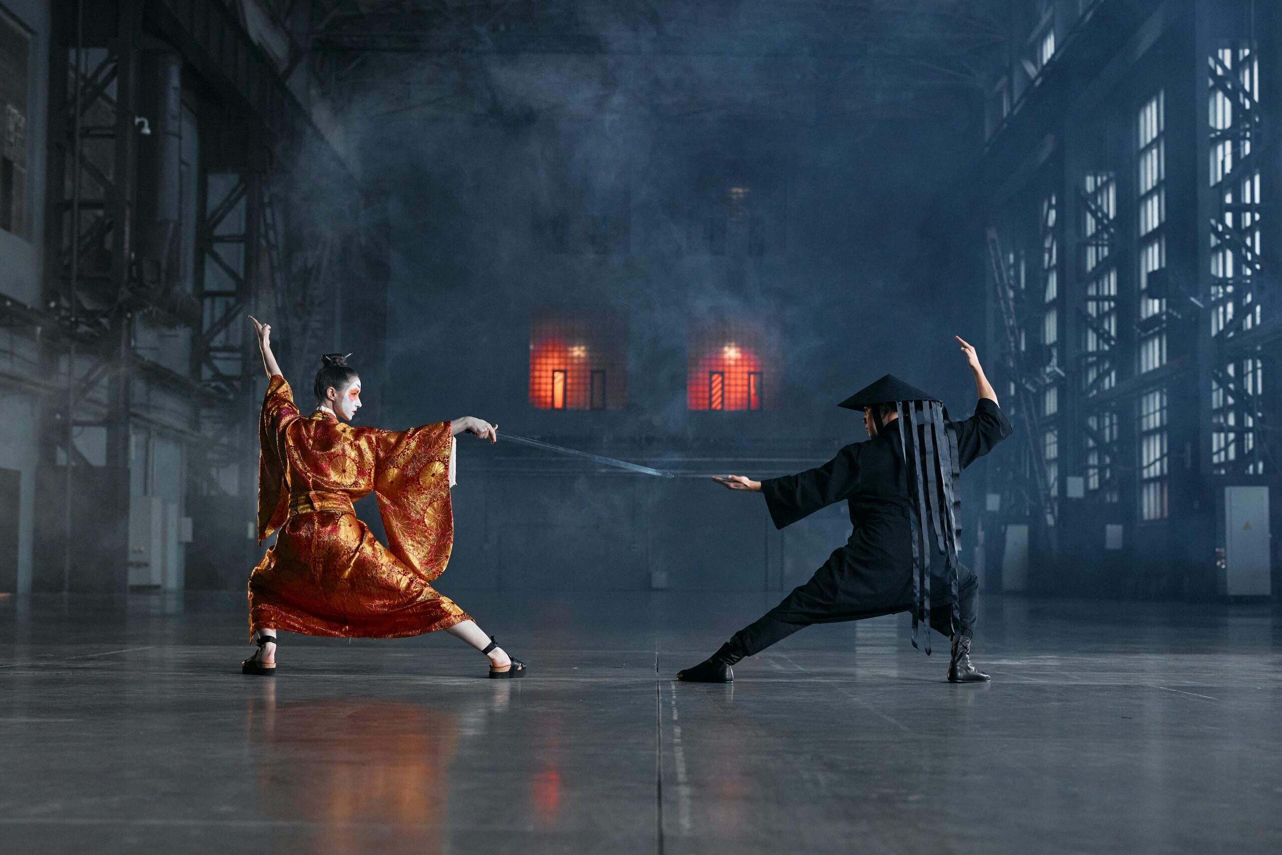 Two cosplayers in an intense martial arts face-off in a dramatic industrial setting.