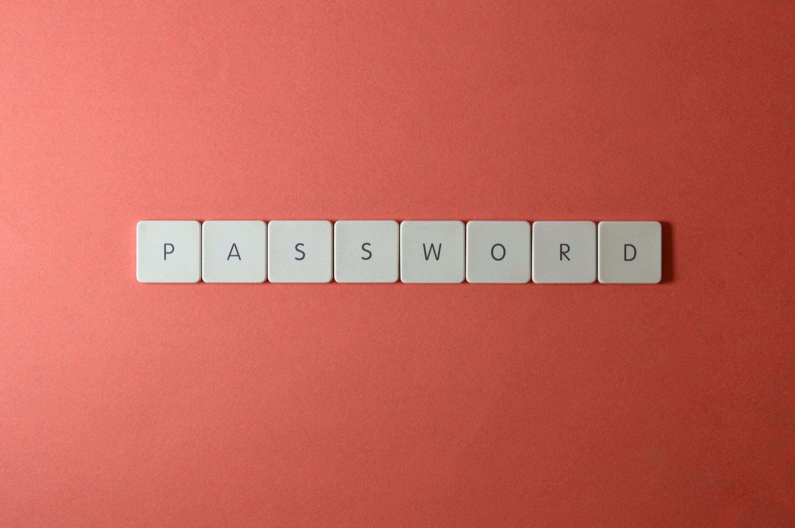 Focus on password security with white keyboard tiles spelling 'PASSWORD' on a coral background.