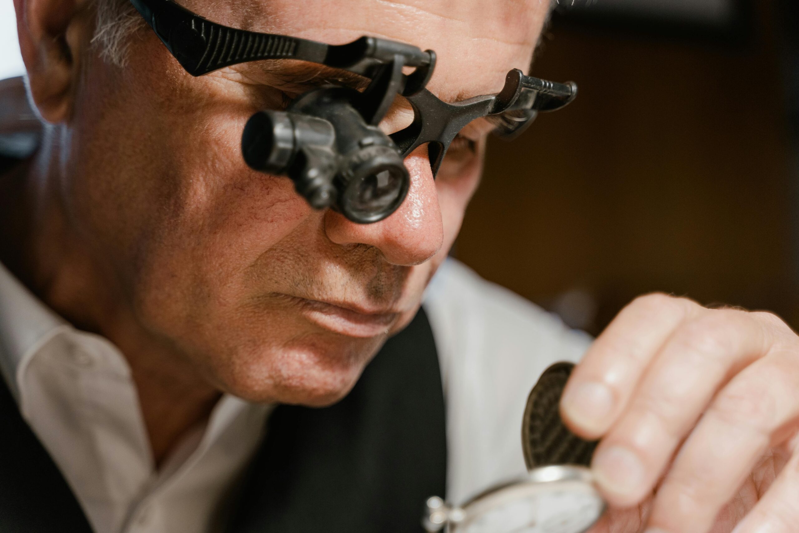 Watchmaker inspects pocket watch using loupe in close-up scene.