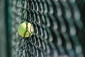 Close-up of a tennis ball trapped in a chain-link fence with selective focus.