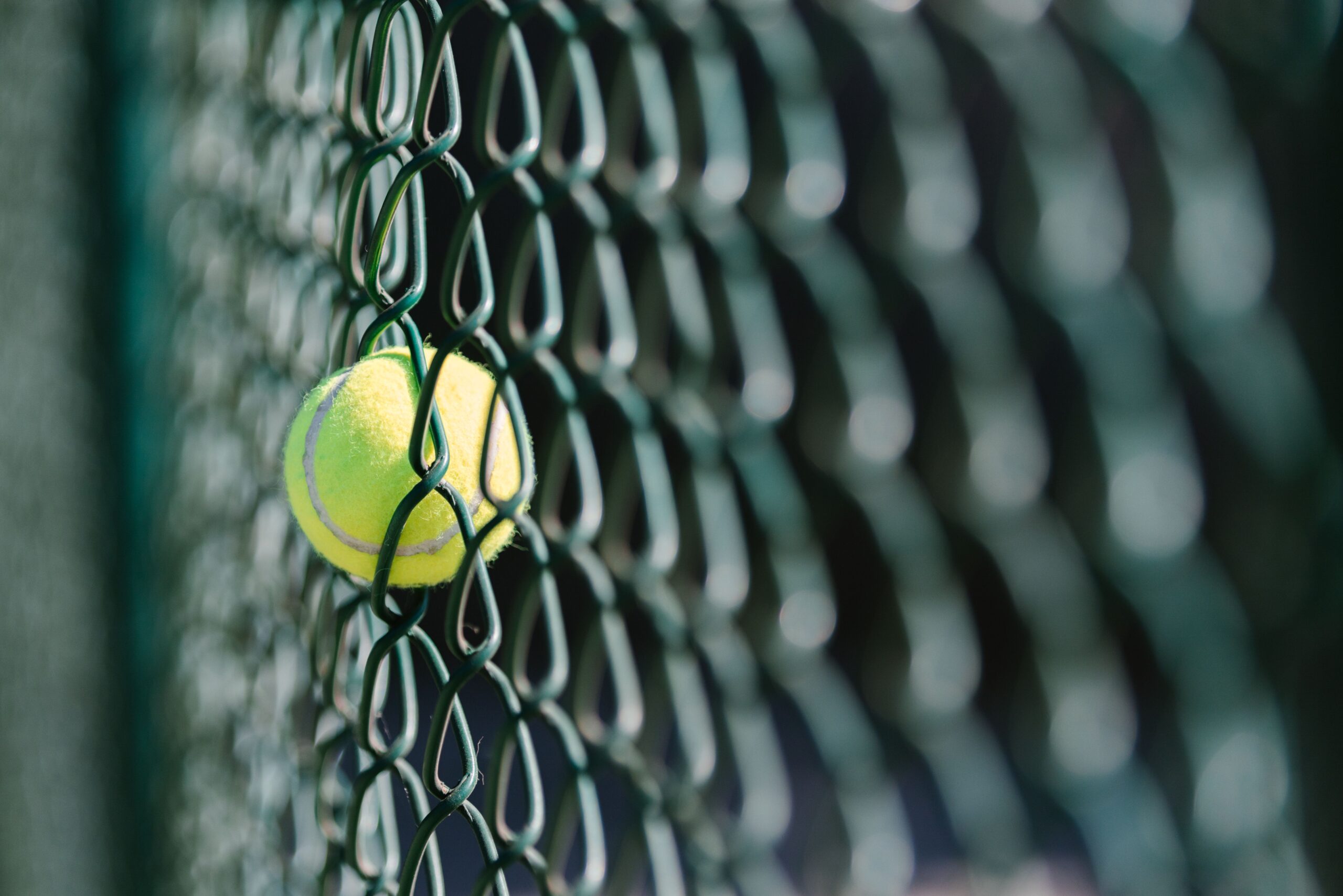 Close-up of a tennis ball trapped in a chain-link fence with selective focus.