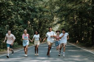 Group of joyful teenagers running and laughing on a forest road during summer.