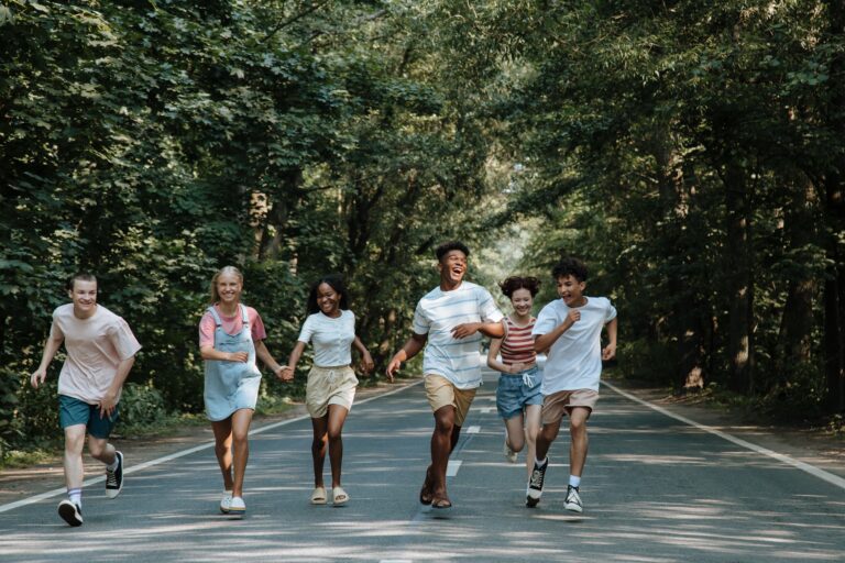 Group of joyful teenagers running and laughing on a forest road during summer.