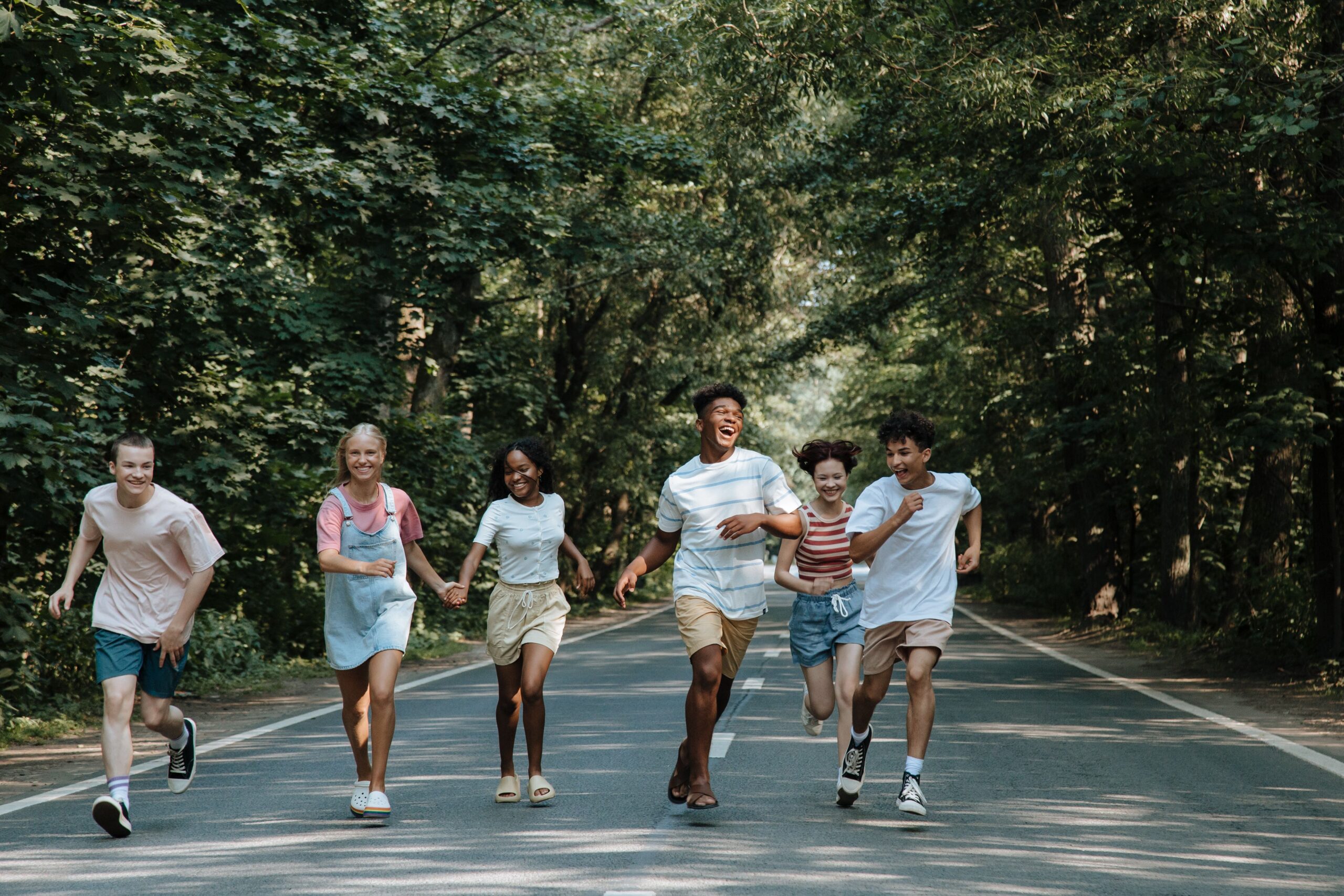 Group of joyful teenagers running and laughing on a forest road during summer.